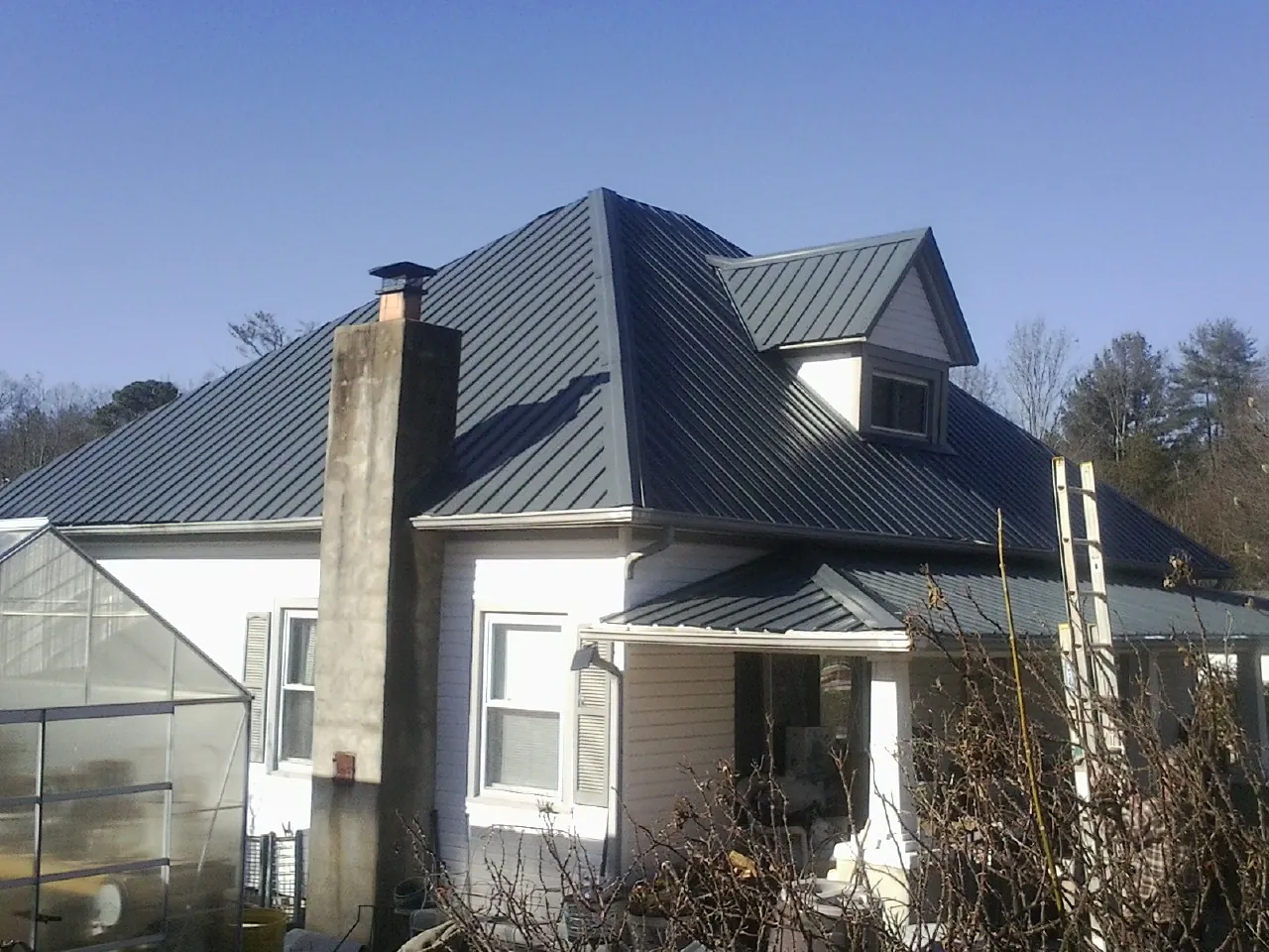 Dark blue standing seam metal roof on a white farmhouse with dormer — Slate & Tile Roof Repair by Roofing Brothers in Bethel Springs