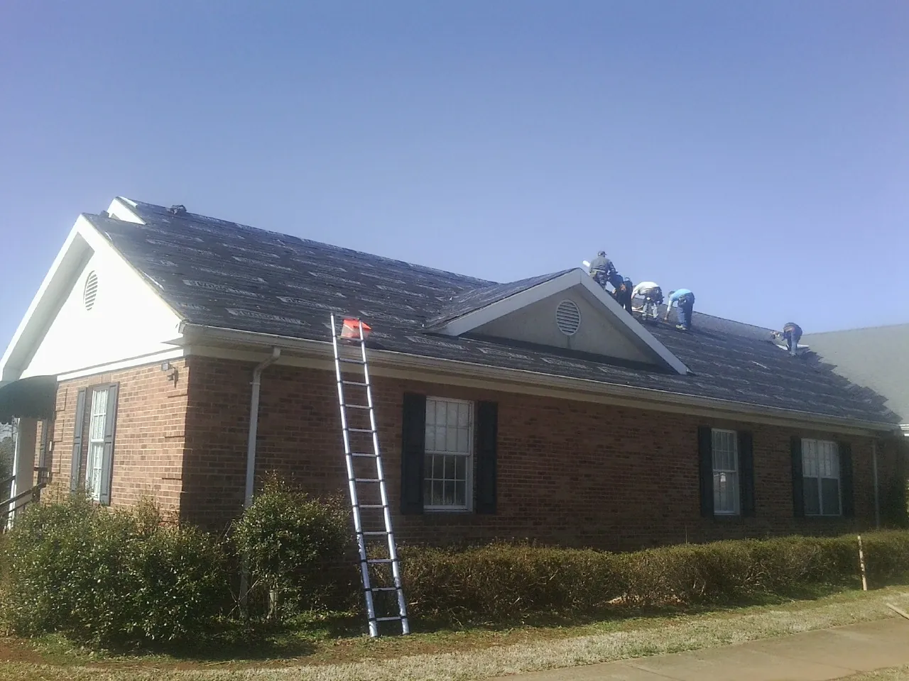 Crew tearing shingles off a brick ranch roof with a ladder set — Emergency Roof Repair work by our crew in Bethel Springs