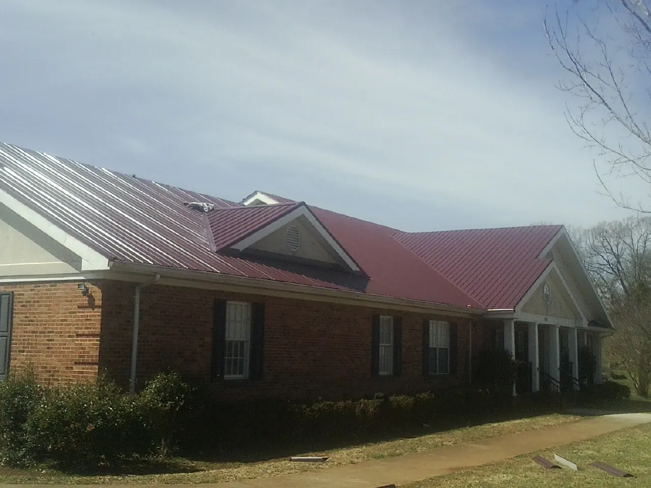 Red metal roof with gabled entries on a long brick building, from a Hail Damage Roof Repair job in Bethel Springs
