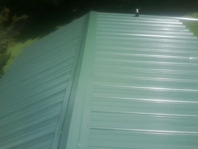 New green metal panels meeting at the ridge of a roof — Flat Roof Repair work by our crew in Bethel Springs