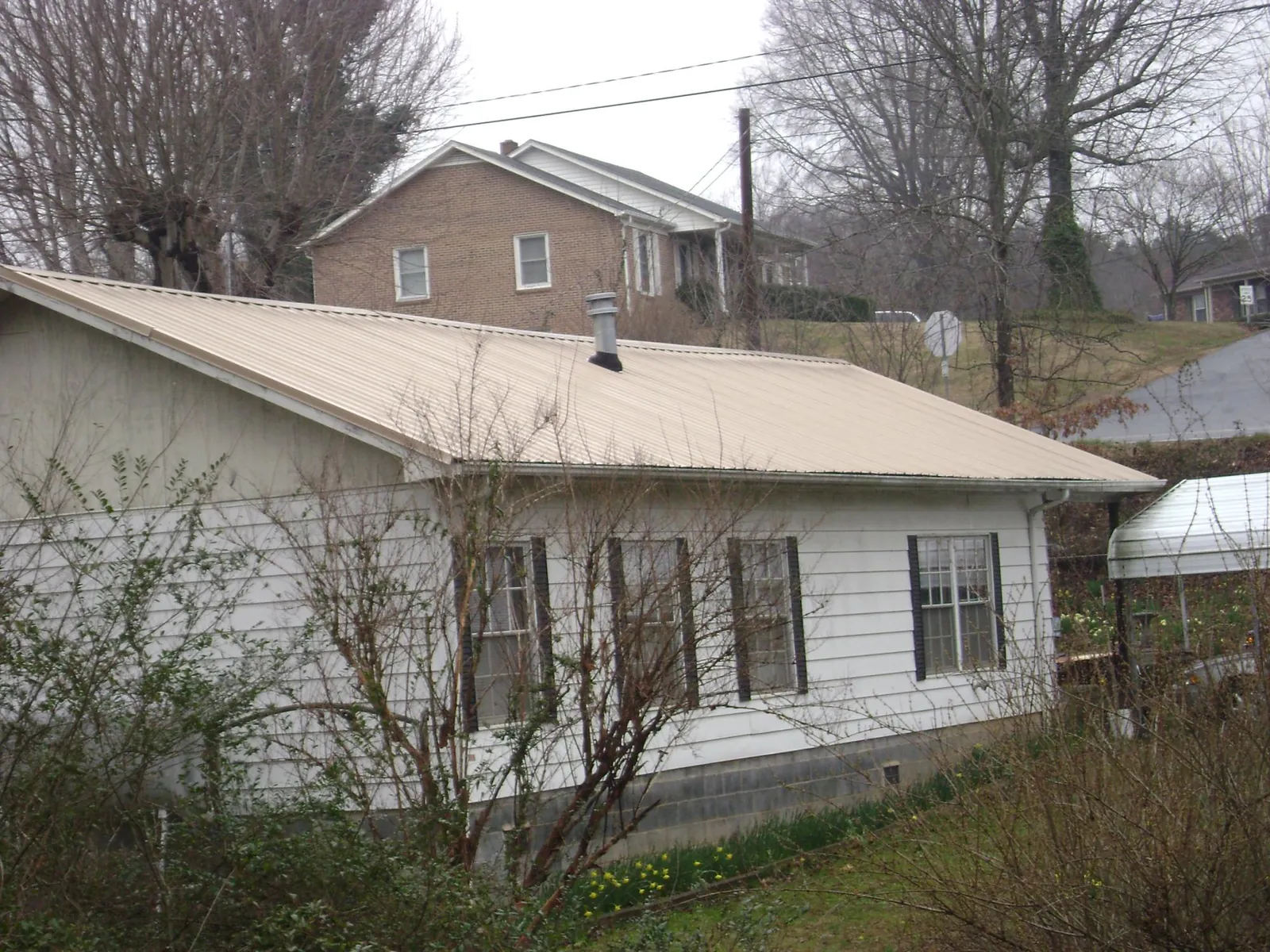 Tan metal roof on a white sided house set into a hillside — Commercial Roofing by Roofing Brothers in Bethel Springs
