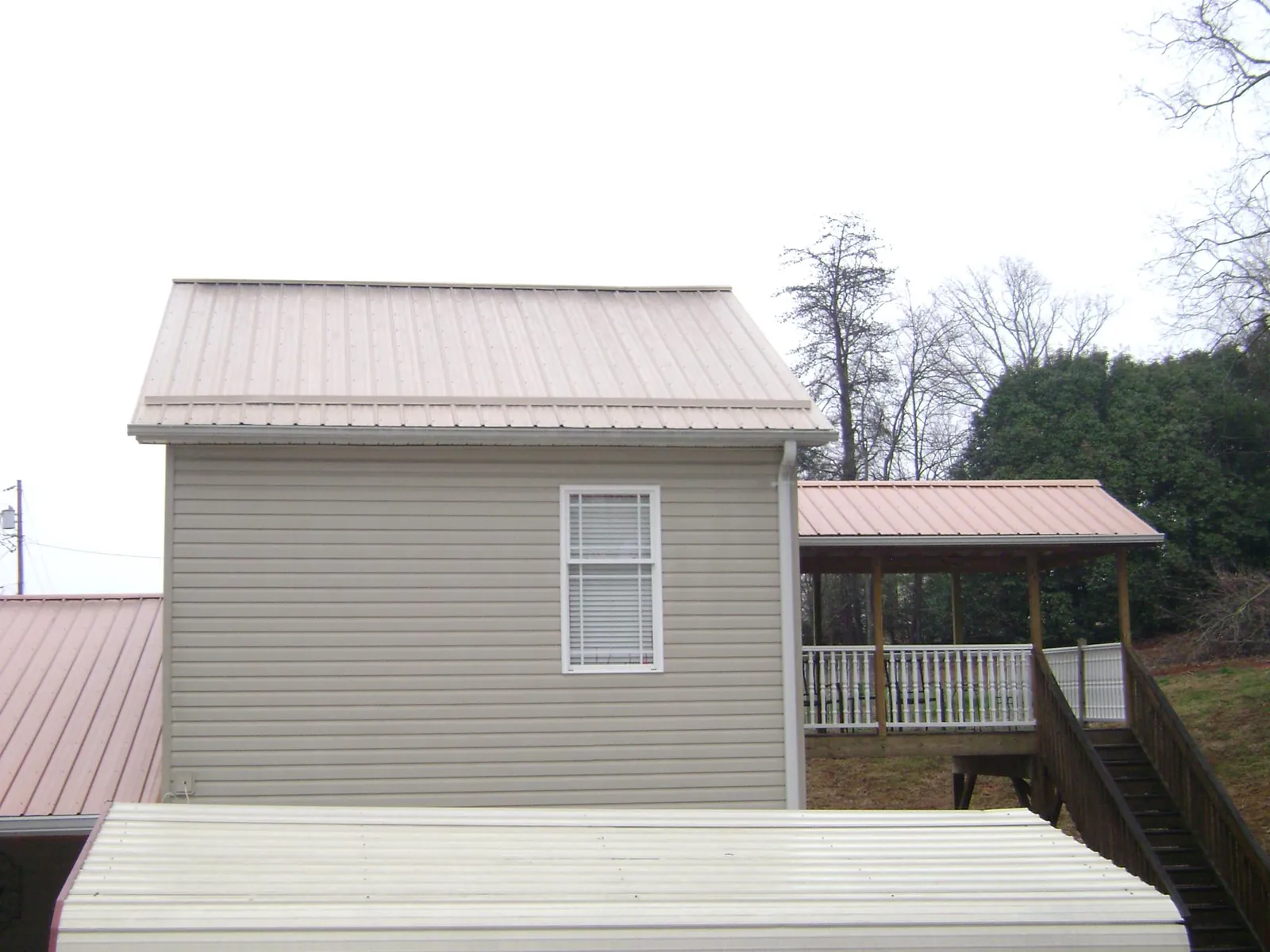 Tan metal roofs on a two story addition and attached porch, from a Roof Replacement job in Bethel Springs